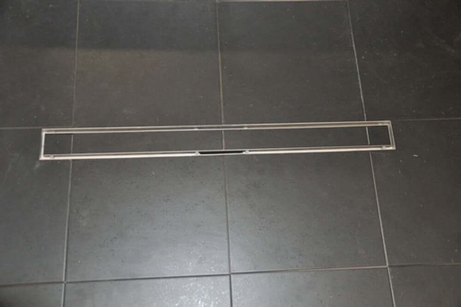 RVS Tegelrooster voor Wiesbaden Douchegoot 50X7 Cm geplaatst op een donkere tegelvloer.